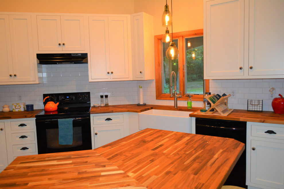Example of a small transitional u-shaped medium tone wood floor and brown floor eat-in kitchen design with a farmhouse sink, recessed-panel cabinets, white cabinets, wood countertops, white backsplash, ceramic backsplash, black appliances, an island and brown countertops