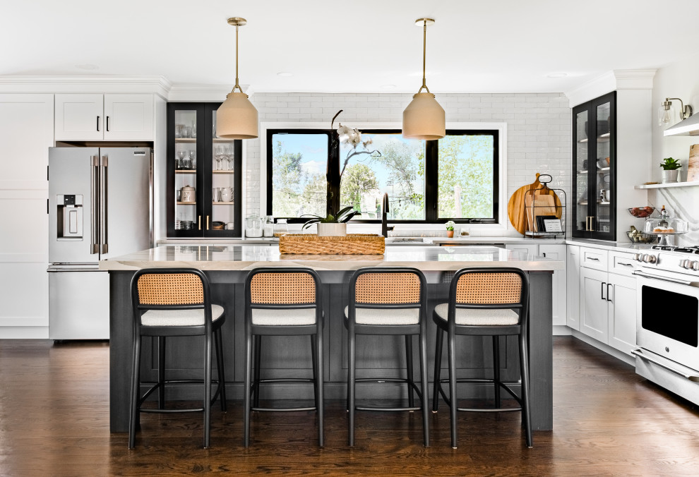 Example of a transitional l-shaped dark wood floor and brown floor kitchen design in Chicago with an undermount sink, shaker cabinets, white cabinets, white backsplash, stainless steel appliances, an island and white countertops