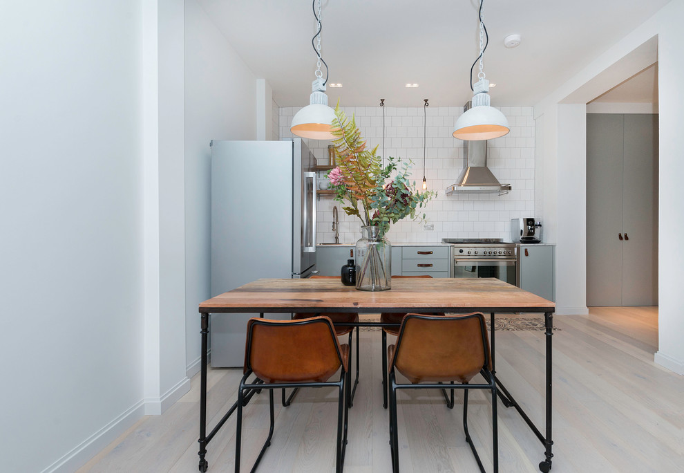 Photo of a scandinavian l-shaped eat-in kitchen in London with flat-panel cabinets, blue cabinets, white splashback, subway tile splashback, stainless steel appliances, light hardwood floors and no island.