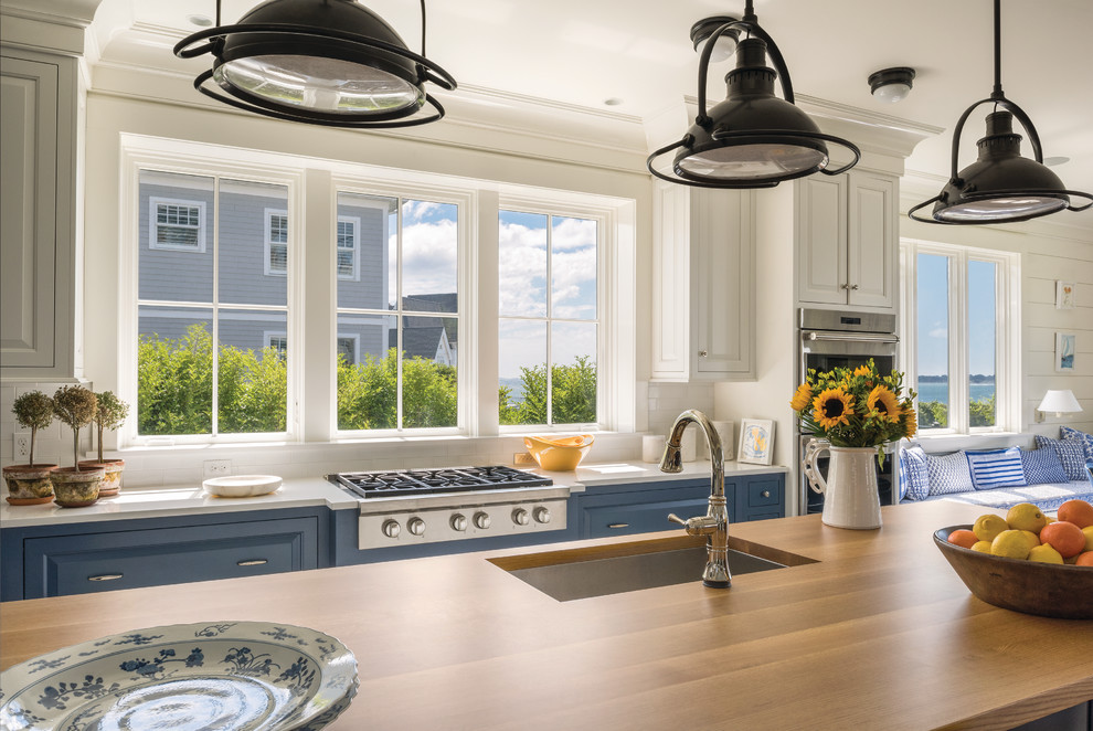 Photo of a large beach style eat-in kitchen in Portland Maine with an undermount sink, white cabinets, wood benchtops, white splashback, subway tile splashback, stainless steel appliances, with island and beige benchtop.