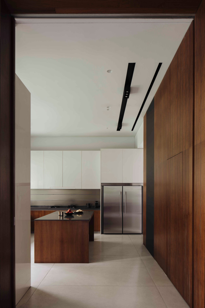 Expansive contemporary u-shaped separate kitchen in Singapore with flat-panel cabinets, medium wood cabinets, stainless steel appliances, with island, beige floor and black benchtop.