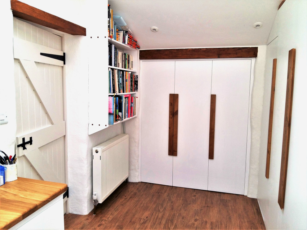 Mittelgroßes Modernes Arbeitszimmer mit Arbeitsplatz, weißer Wandfarbe, braunem Holzboden, Einbau-Schreibtisch, braunem Boden und freigelegten Dachbalken in Cornwall