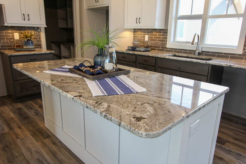 Eat-in kitchen - mid-sized transitional l-shaped laminate floor and brown floor eat-in kitchen idea in Minneapolis with an undermount sink, shaker cabinets, white cabinets, granite countertops, gray backsplash, ceramic backsplash, an island and multicolored countertops