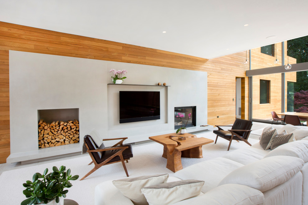 На фото: большая открытая гостиная комната в стиле модернизм с бежевыми стенами, полом из известняка, стандартным камином, фасадом камина из бетона, телевизором на стене, серым полом и деревянными стенами с