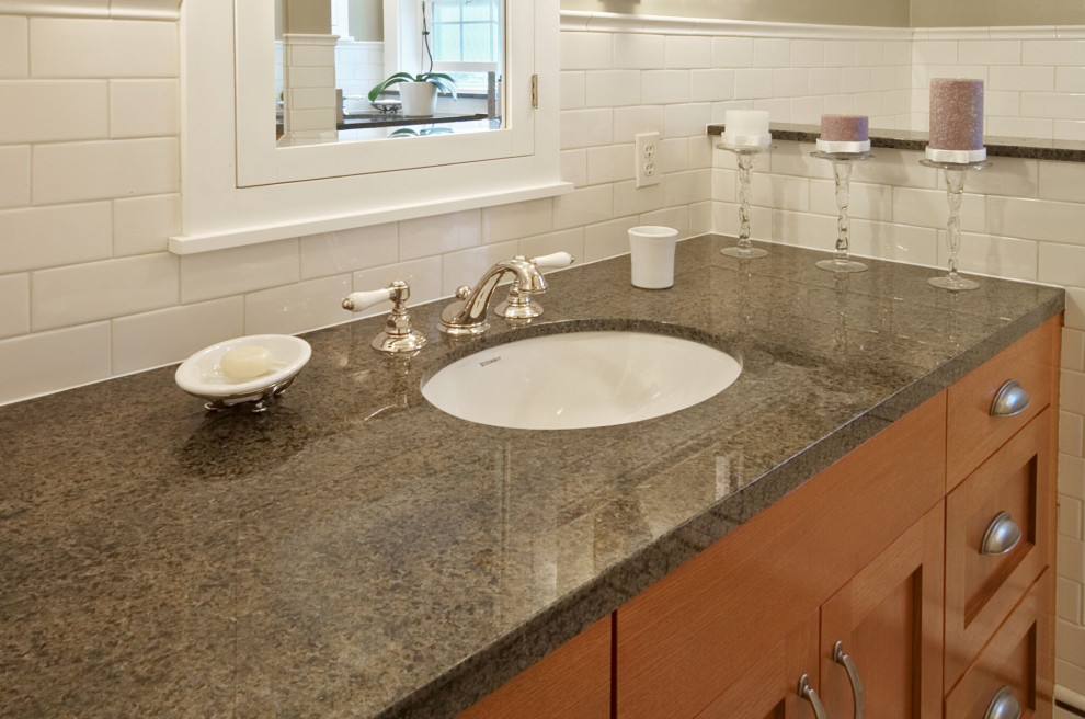 This is an example of an arts and crafts bathroom in Seattle with medium wood cabinets, white tile, subway tile, beige walls, ceramic floors, an undermount sink, granite benchtops, white floor and black benchtops.