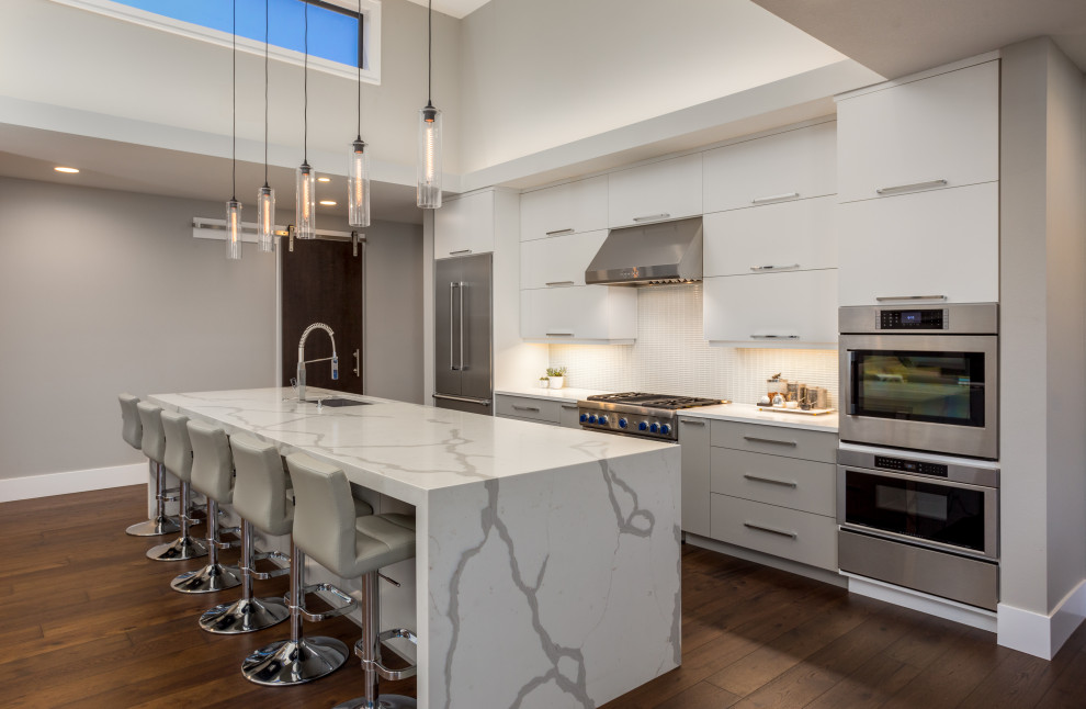 Photo of a large contemporary galley kitchen in Houston with flat-panel cabinets, quartz benchtops, white splashback, ceramic splashback, white benchtop, an undermount sink, grey cabinets, stainless steel appliances, medium hardwood floors, with island and brown floor.