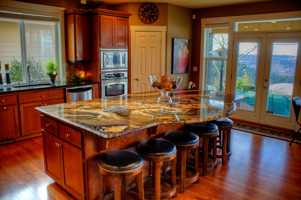 Photo of a large traditional l-shaped eat-in kitchen in Seattle with a drop-in sink, granite benchtops, beige splashback, recessed-panel cabinets, medium wood cabinets, stone tile splashback, stainless steel appliances, medium hardwood floors and with island.