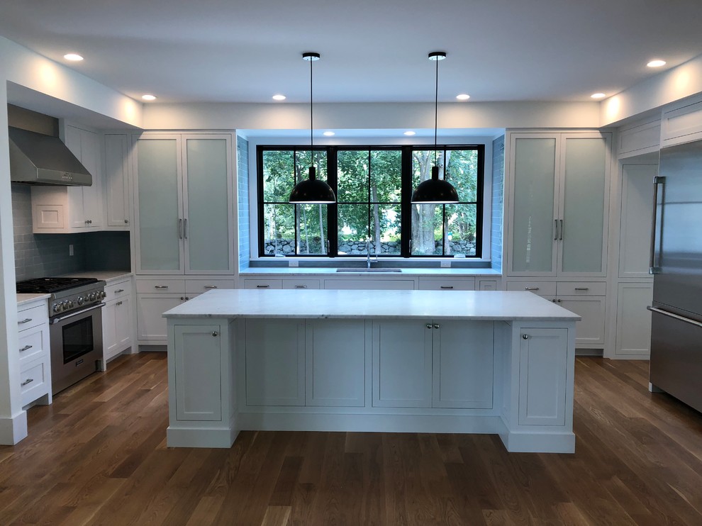 This is an example of a large country u-shaped eat-in kitchen in Other with an undermount sink, recessed-panel cabinets, white cabinets, marble benchtops, grey splashback, subway tile splashback, stainless steel appliances, medium hardwood floors, with island, brown floor and white benchtop.
