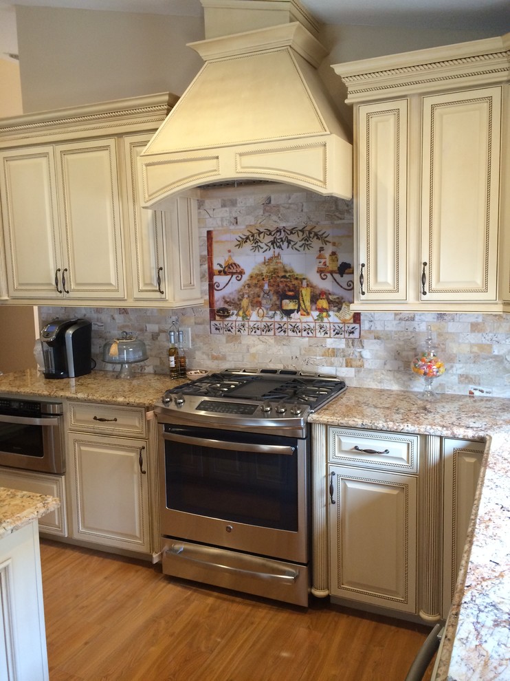 Photo of a large arts and crafts u-shaped kitchen pantry in Tampa with an undermount sink, raised-panel cabinets, beige cabinets, granite benchtops, beige splashback, terra-cotta splashback, stainless steel appliances, light hardwood floors and with island.