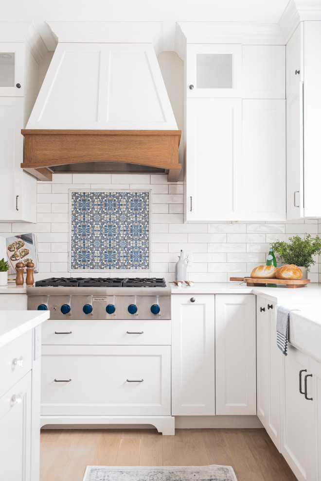 Mid-sized transitional light wood floor kitchen photo in Minneapolis with a farmhouse sink, white cabinets, stainless steel appliances and an island