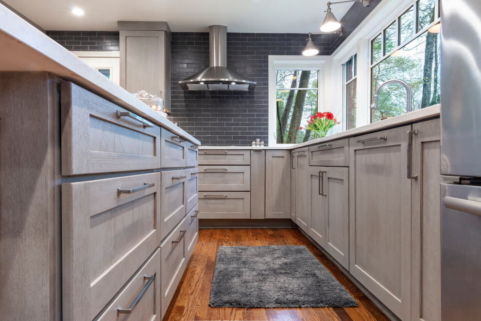Example of a trendy u-shaped medium tone wood floor and brown floor eat-in kitchen design with an undermount sink, shaker cabinets, gray cabinets, quartz countertops, gray backsplash, ceramic backsplash, stainless steel appliances, an island and gray countertops