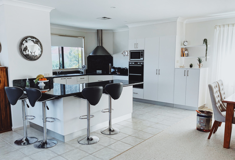 This is an example of a mid-sized contemporary u-shaped open plan kitchen in Newcastle - Maitland with flat-panel cabinets, white cabinets, laminate benchtops, black splashback, stainless steel appliances, a peninsula and black benchtop.