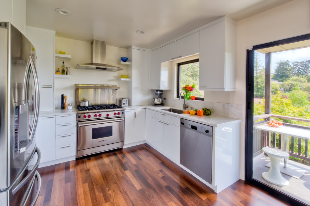 Design ideas for a small contemporary u-shaped kitchen in San Francisco with stainless steel appliances, an undermount sink, flat-panel cabinets, white cabinets, marble benchtops, white splashback, subway tile splashback, medium hardwood floors, no island and beige floor.