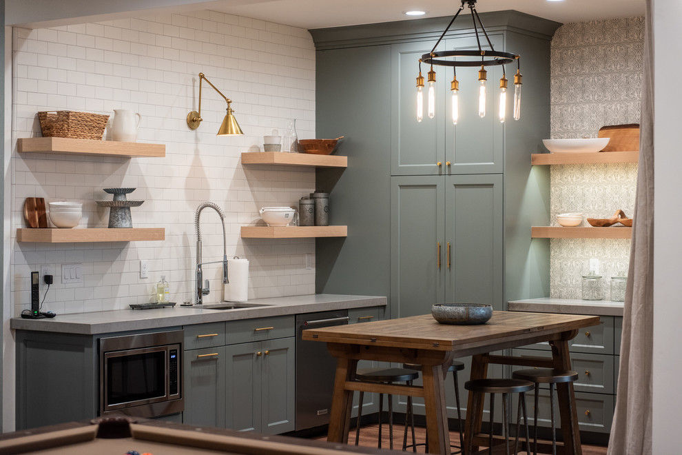Inspiration for a country l-shaped seated home bar in Salt Lake City with an undermount sink, shaker cabinets, green cabinets, white splashback, subway tile splashback, medium hardwood floors, brown floor and grey benchtop.