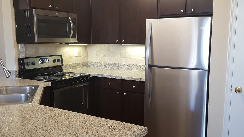 This is an example of a small transitional u-shaped separate kitchen in Dallas with a drop-in sink, flat-panel cabinets, brown cabinets, quartz benchtops, beige splashback, travertine splashback, black appliances, travertine floors, with island and beige floor.