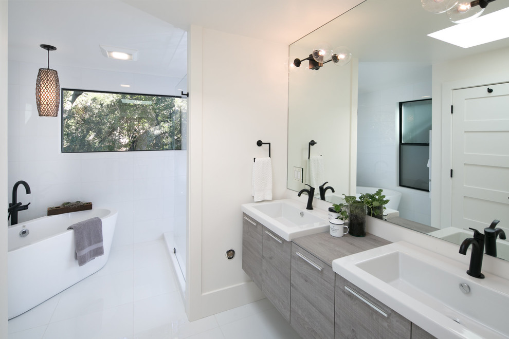 This is an example of a large midcentury master bathroom in San Francisco with flat-panel cabinets, light wood cabinets, a freestanding tub, an alcove shower, a one-piece toilet, white tile, marble, white walls, marble floors, a wall-mount sink, solid surface benchtops, white floor and an open shower.