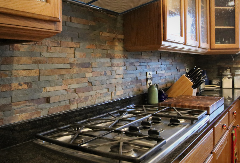 Eat-in kitchen - mid-sized rustic l-shaped eat-in kitchen idea with glass-front cabinets, light wood cabinets, granite countertops, multicolored backsplash, stone tile backsplash, stainless steel appliances, an island and black countertops