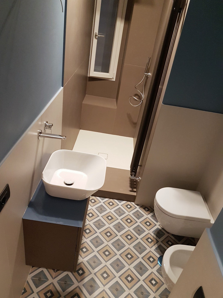 Пример оригинального дизайна: маленькая ванная комната в современном стиле с плоскими фасадами, коричневыми фасадами, душем без бортиков, раздельным унитазом, бежевой плиткой, керамогранитной плиткой, синими стенами, полом из керамогранита, настольной раковиной, стеклянной столешницей, синей столешницей, тумбой под одну раковину и подвесной тумбой для на участке и в саду