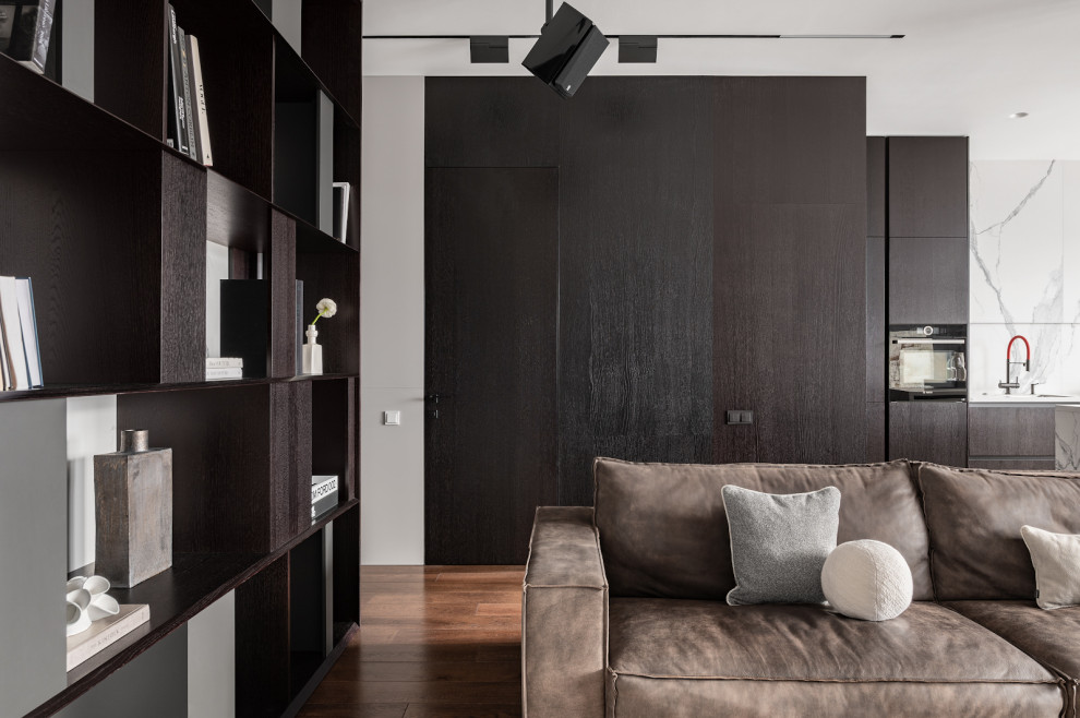 На фото: серо-белая гостиная комната среднего размера в современном стиле с паркетным полом среднего тона, панелями на стенах, с книжными шкафами и полками, белыми стенами и коричневым диваном без телевизора