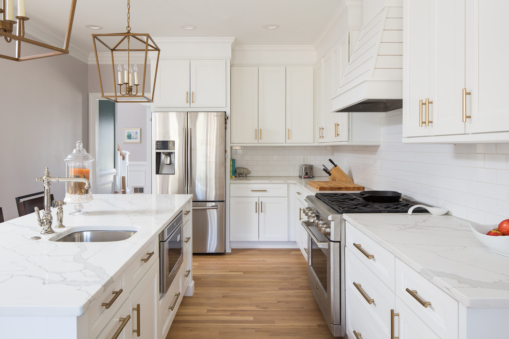 This is an example of a mid-sized contemporary u-shaped eat-in kitchen in Atlanta with a farmhouse sink, recessed-panel cabinets, white cabinets, quartz benchtops, white splashback, ceramic splashback, stainless steel appliances, light hardwood floors, with island and white benchtop.