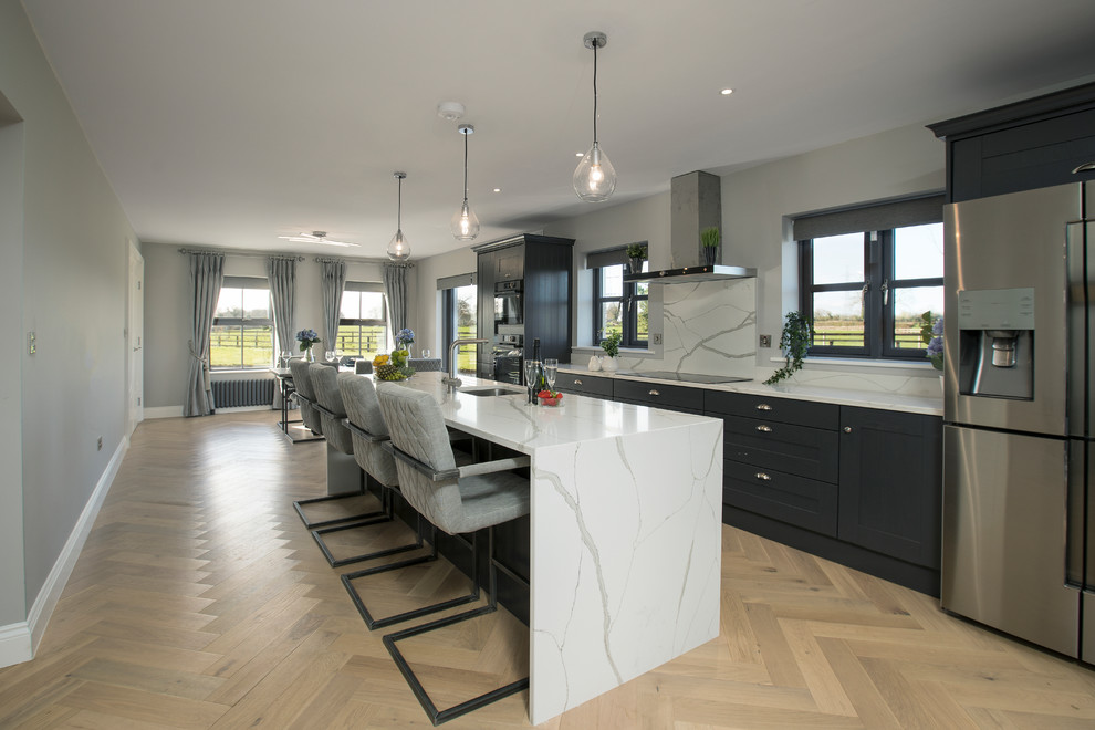 This is an example of a large contemporary single-wall eat-in kitchen in Dublin with a drop-in sink, shaker cabinets, grey cabinets, quartzite benchtops, white splashback, stone slab splashback, panelled appliances, medium hardwood floors, with island, grey floor and white benchtop.