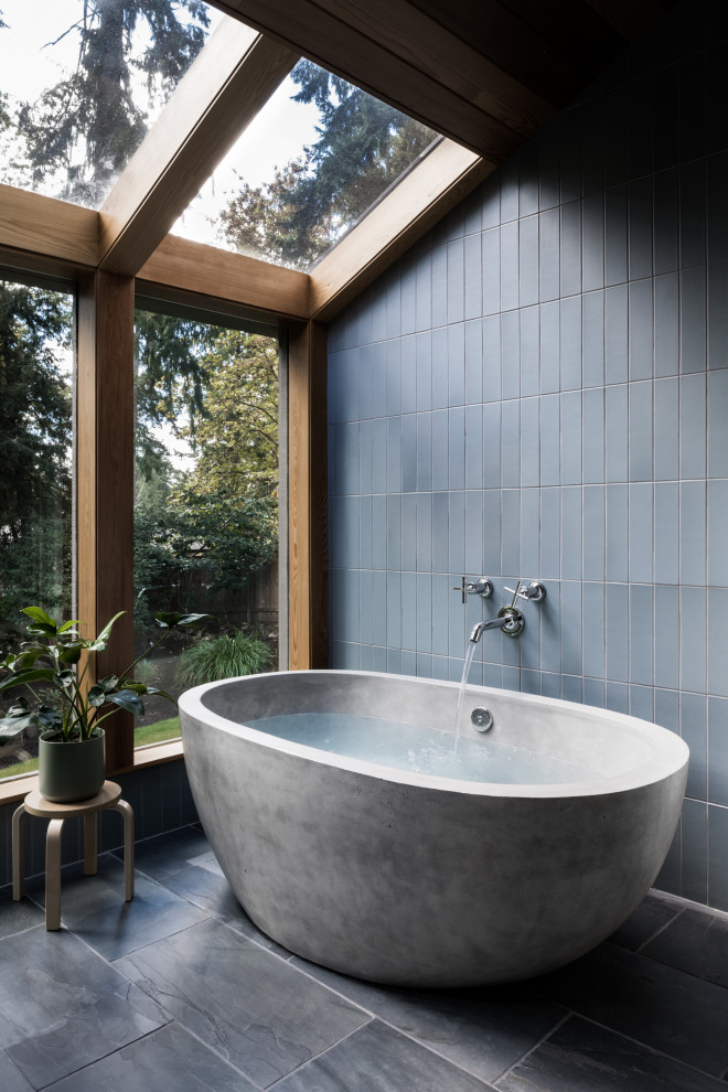 This is an example of a midcentury master bathroom in Portland with flat-panel cabinets, medium wood cabinets, a freestanding tub, blue tile, ceramic tile, slate floors, an integrated sink, concrete benchtops, grey floor, grey benchtops, an enclosed toilet, a double vanity, a floating vanity and wood walls.