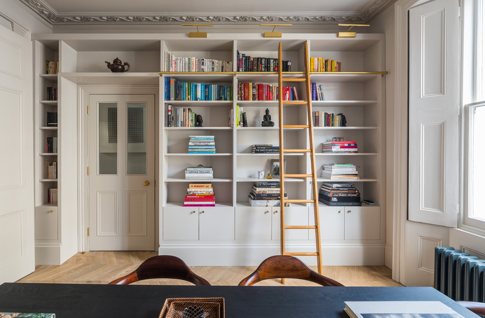 This is an example of a mid-sized traditional home office in London with white walls and light hardwood floors.