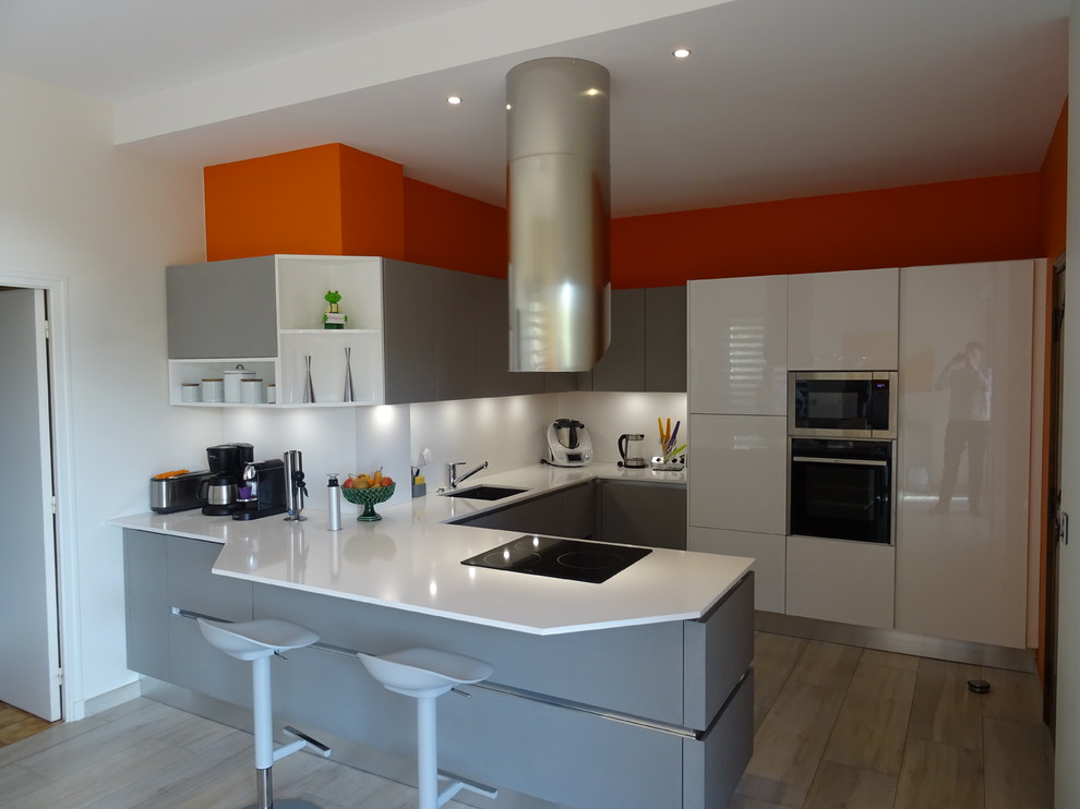 This is an example of a large modern u-shaped eat-in kitchen in Marseille with an integrated sink, beaded inset cabinets, grey cabinets, quartzite benchtops, white splashback, stainless steel appliances, ceramic floors, a peninsula, brown floor and white benchtop.