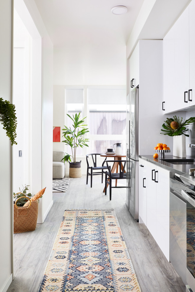 This is an example of a small contemporary galley eat-in kitchen in San Francisco with flat-panel cabinets, white cabinets, quartzite benchtops, grey splashback, ceramic splashback, stainless steel appliances, vinyl floors, no island, grey floor, an undermount sink and grey benchtop.