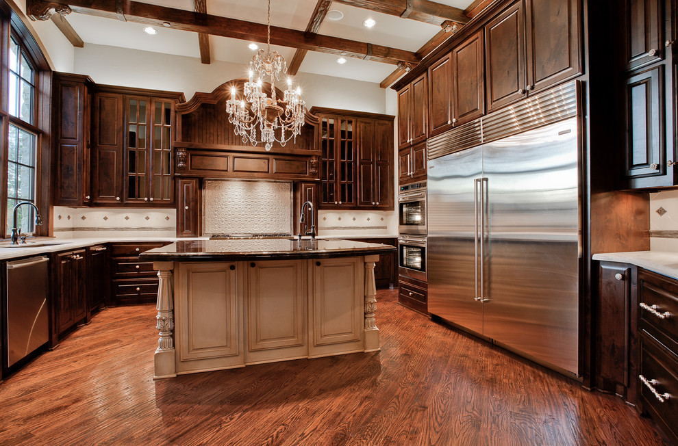 This is an example of a large traditional u-shaped separate kitchen in Dallas with an undermount sink, raised-panel cabinets, dark wood cabinets, marble benchtops, beige splashback, ceramic splashback, stainless steel appliances, medium hardwood floors, with island and brown floor.