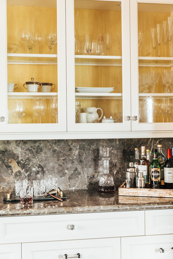 Inspiration for a mid-sized transitional single-wall home bar in Other with glass-front cabinets, white cabinets, limestone benchtops, limestone splashback, medium hardwood floors and multi-coloured benchtop.