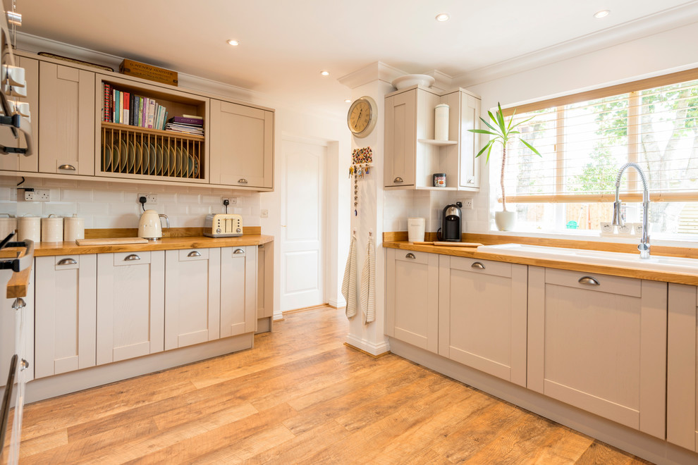 Photo of a mid-sized country kitchen in Dorset with a double-bowl sink, shaker cabinets, beige cabinets, wood benchtops, timber splashback, stainless steel appliances, laminate floors and brown floor.