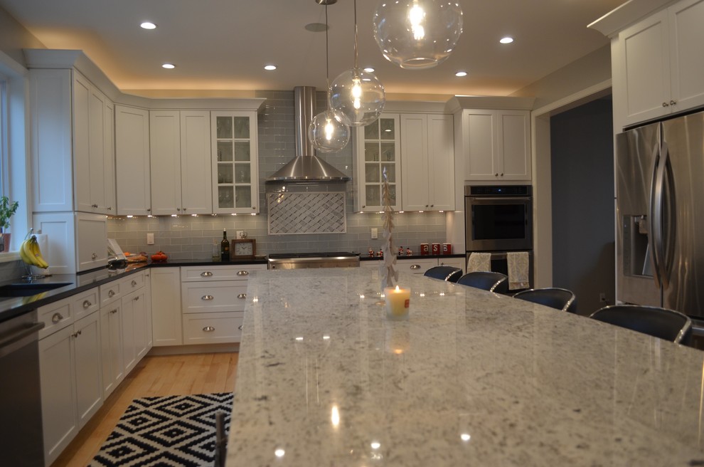 Mid-sized transitional single-wall light wood floor and yellow floor eat-in kitchen photo with an undermount sink, shaker cabinets, white cabinets, quartz countertops, gray backsplash, glass tile backsplash, stainless steel appliances and an island