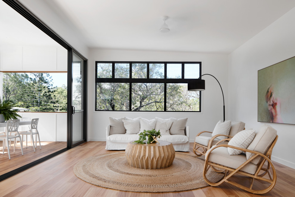 This is an example of a beach style living room in Brisbane with white walls, light hardwood floors and beige floor.