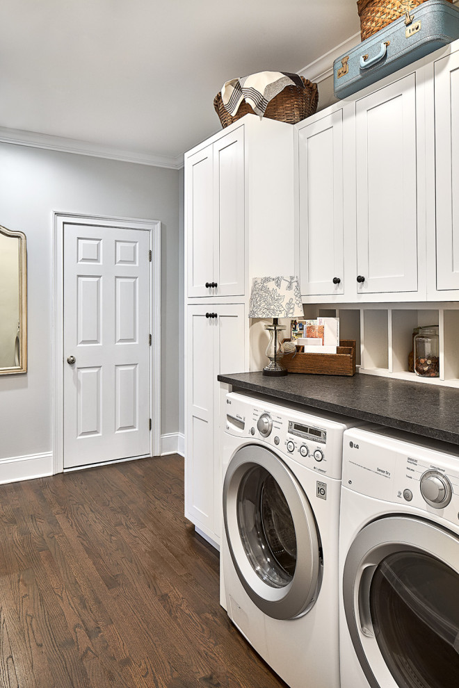 Photo of a mid-sized country single-wall dedicated laundry room in Charlotte with shaker cabinets, white cabinets, granite benchtops, grey walls, dark hardwood floors, a side-by-side washer and dryer, brown floor and black benchtop.