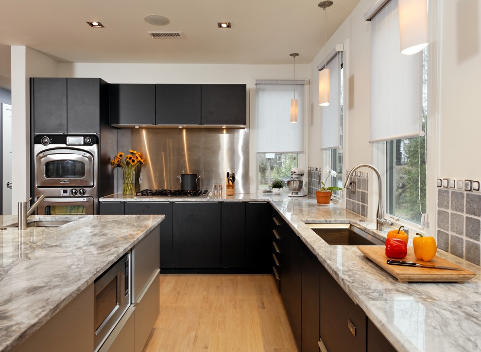 Design ideas for a mid-sized transitional l-shaped eat-in kitchen in DC Metro with stainless steel appliances, a single-bowl sink, flat-panel cabinets, black cabinets, metallic splashback, metal splashback, granite benchtops, light hardwood floors, with island and beige floor.