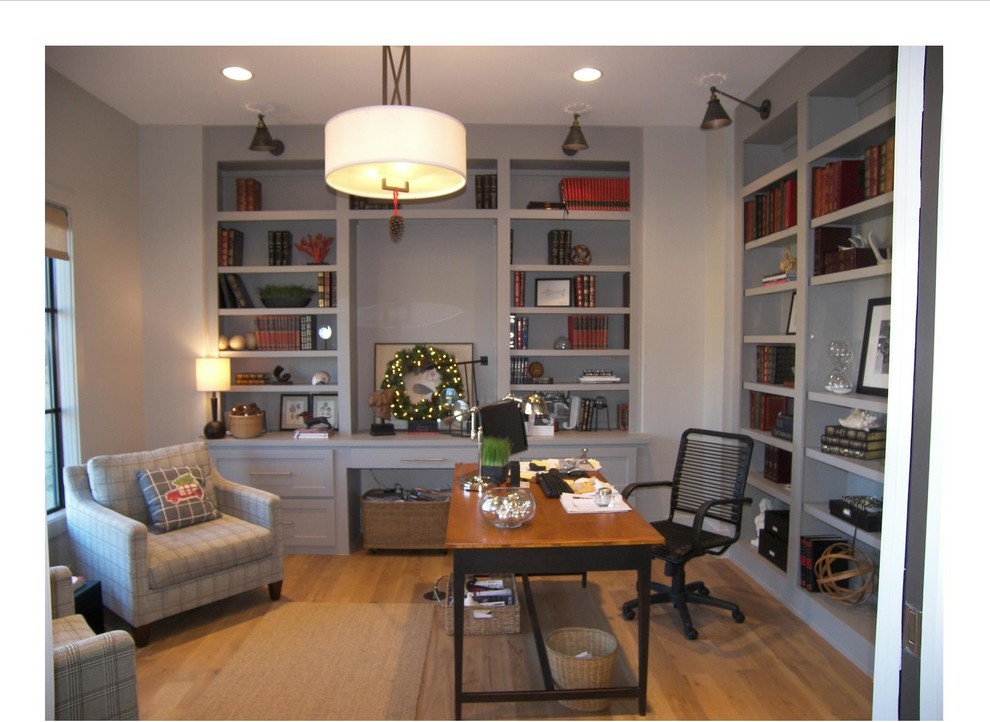 This is an example of an industrial home office in Dallas with grey walls, light hardwood floors, a built-in desk and a library.