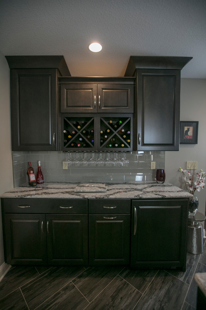 Large contemporary galley seated home bar in Kansas City with an undermount sink, raised-panel cabinets, dark wood cabinets, solid surface benchtops, grey splashback, subway tile splashback, vinyl floors and grey floor.