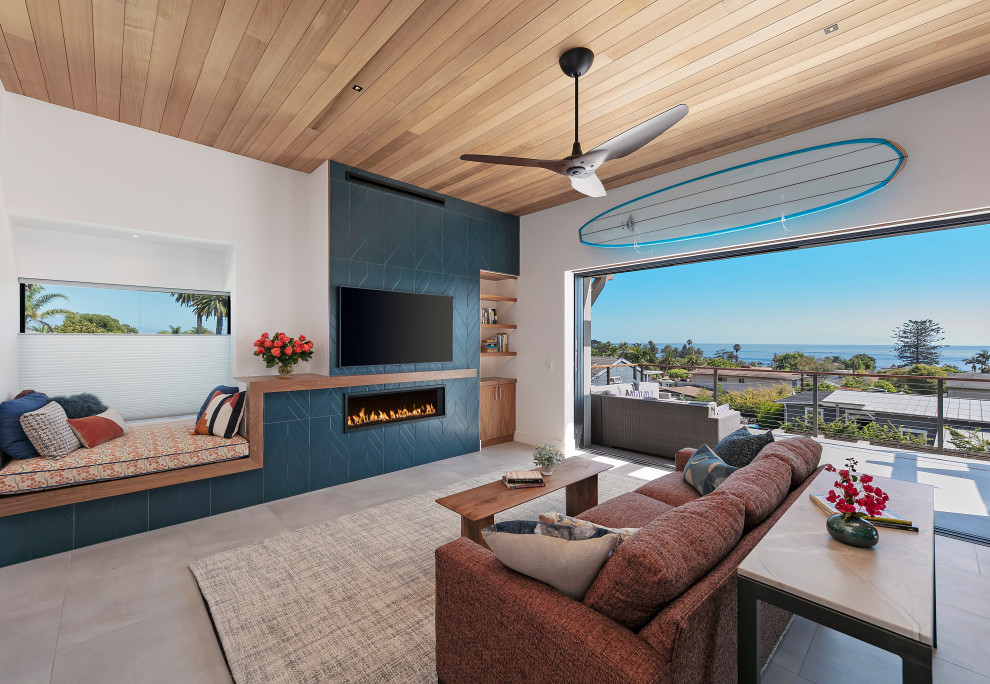 サンタバーバラにある高級な中くらいなビーチスタイルのおしゃれなLDK (白い壁、磁器タイルの床、横長型暖炉、タイルの暖炉まわり、壁掛け型テレビ、ベージュの床、板張り天井) の写真