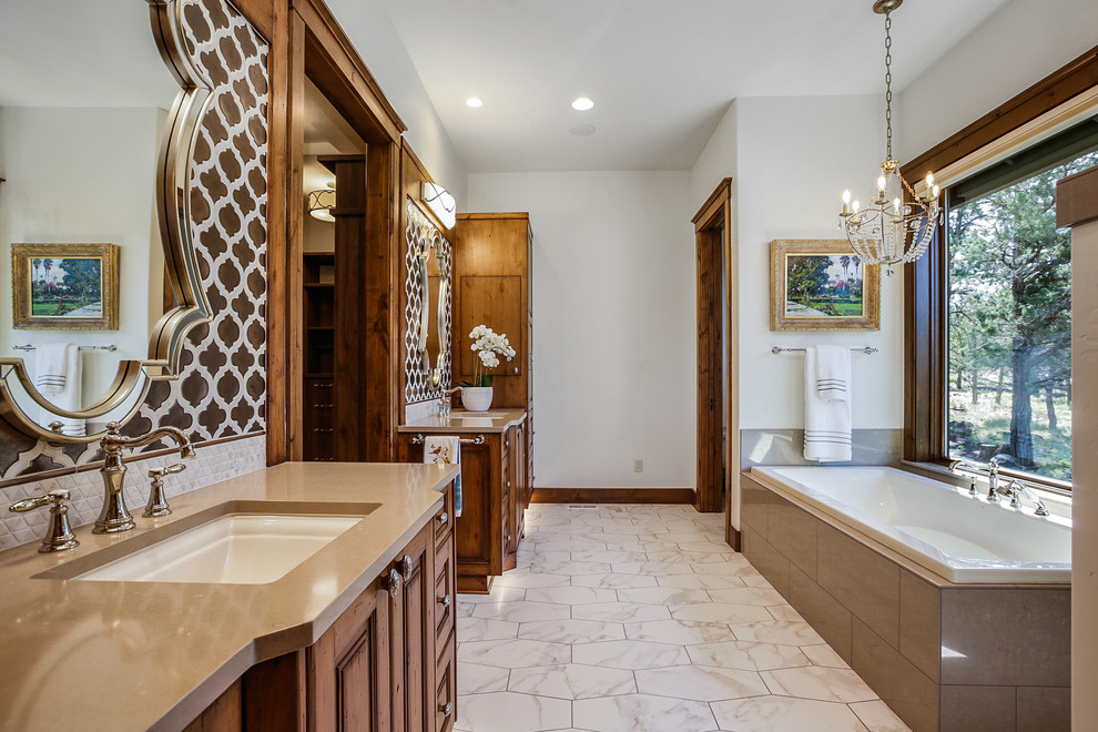 Photo of a mid-sized country master bathroom in Other with beaded inset cabinets, distressed cabinets, a drop-in tub, a curbless shower, a two-piece toilet, beige tile, ceramic tile, beige walls, ceramic floors, an undermount sink, engineered quartz benchtops, multi-coloured floor, an open shower and brown benchtops.