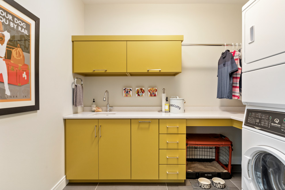 Design ideas for a mid-sized contemporary l-shaped dedicated laundry room in Other with an undermount sink, flat-panel cabinets, yellow cabinets, white walls, a stacked washer and dryer, grey floor, white benchtop, quartz benchtops and porcelain floors.