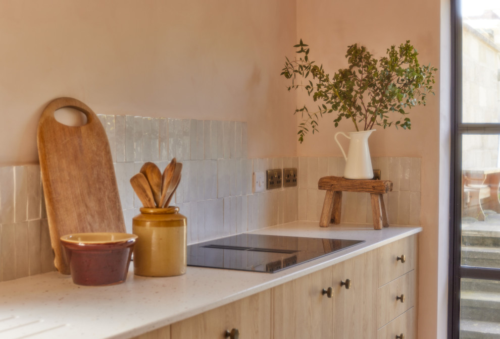 Foto di una grande cucina mediterranea con lavello sottopiano, ante lisce, ante in legno chiaro, top in superficie solida, paraspruzzi beige, paraspruzzi con piastrelle in ceramica, elettrodomestici neri, pavimento in cemento, penisola, pavimento rosa e top beige