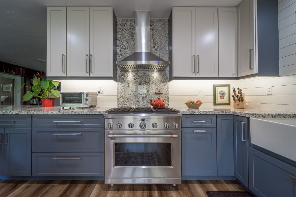 Design ideas for a large country l-shaped kitchen pantry in Miami with a farmhouse sink, shaker cabinets, blue cabinets, granite benchtops, beige splashback, shiplap splashback, stainless steel appliances, vinyl floors, a peninsula, brown floor and multi-coloured benchtop.