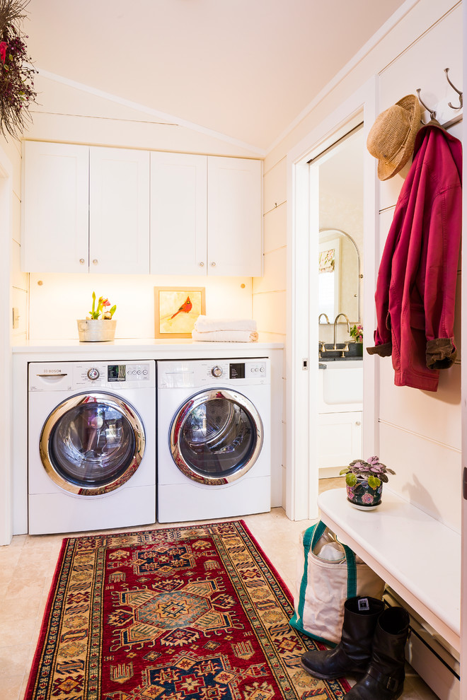 Design ideas for a mid-sized transitional single-wall utility room in Burlington with a side-by-side washer and dryer, shaker cabinets, white cabinets, solid surface benchtops, white walls and travertine floors.