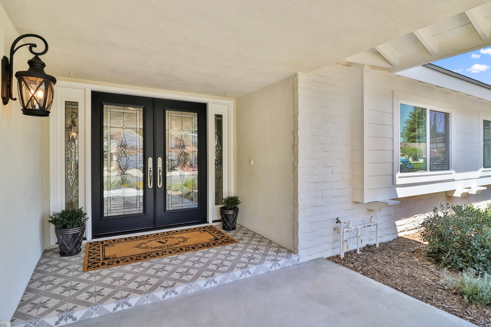This is an example of a mid-sized transitional front door in Los Angeles with beige walls, ceramic floors, a double front door, a black front door, grey floor and brick walls.