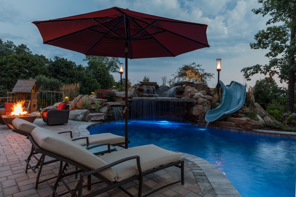 Design ideas for a mid-sized country backyard custom-shaped pool in New York with a water slide and brick pavers.
