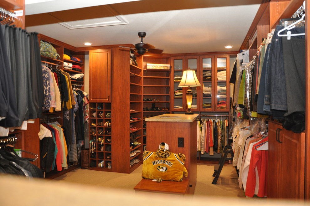 This is an example of an expansive traditional walk-in wardrobe in Other with raised-panel cabinets, medium wood cabinets and carpet.
