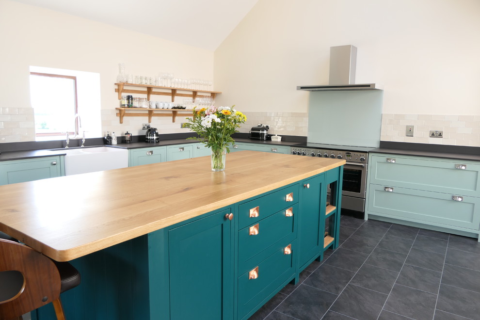 Inspiration for a large traditional l-shaped open plan kitchen in West Midlands with a farmhouse sink, shaker cabinets, green cabinets, quartz benchtops, grey splashback, glass sheet splashback, stainless steel appliances, ceramic floors, with island, black floor and black benchtop.