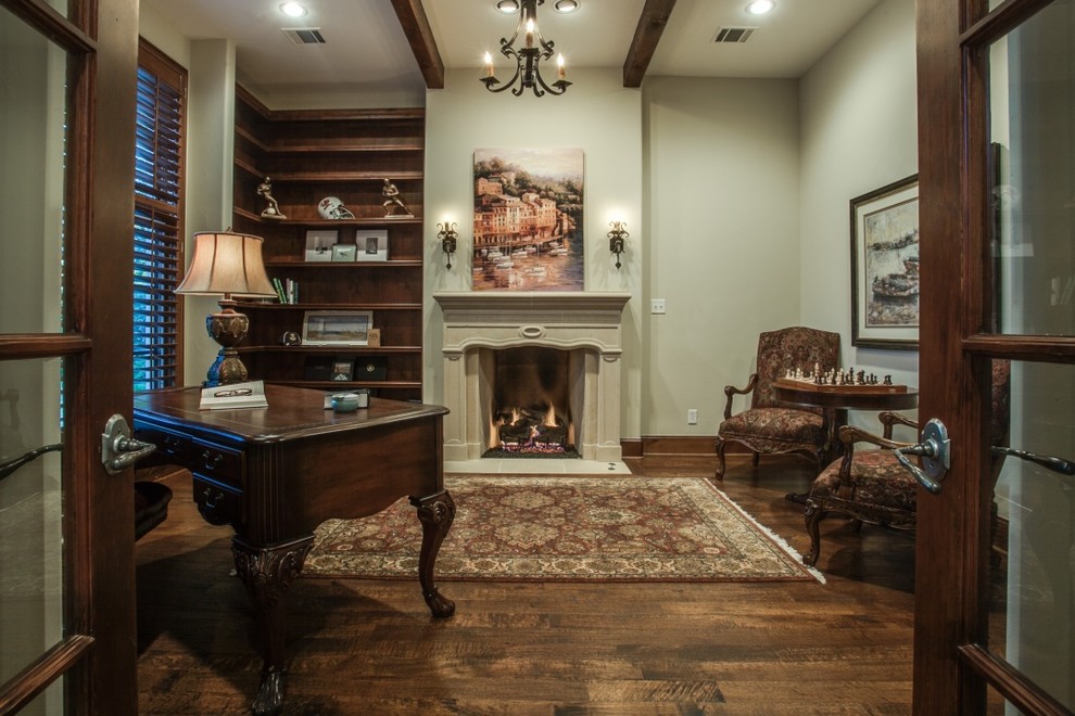 Inspiration for a mid-sized traditional study room in Dallas with beige walls, dark hardwood floors, a standard fireplace, a plaster fireplace surround, a freestanding desk and brown floor.