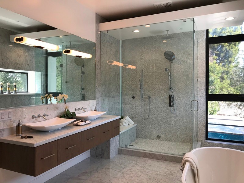 Design ideas for a large contemporary master bathroom in Los Angeles with beaded inset cabinets, dark wood cabinets, a freestanding tub, a corner shower, gray tile, pebble tile, grey walls, marble floors, a vessel sink, marble benchtops, grey floor, a hinged shower door and grey benchtops.
